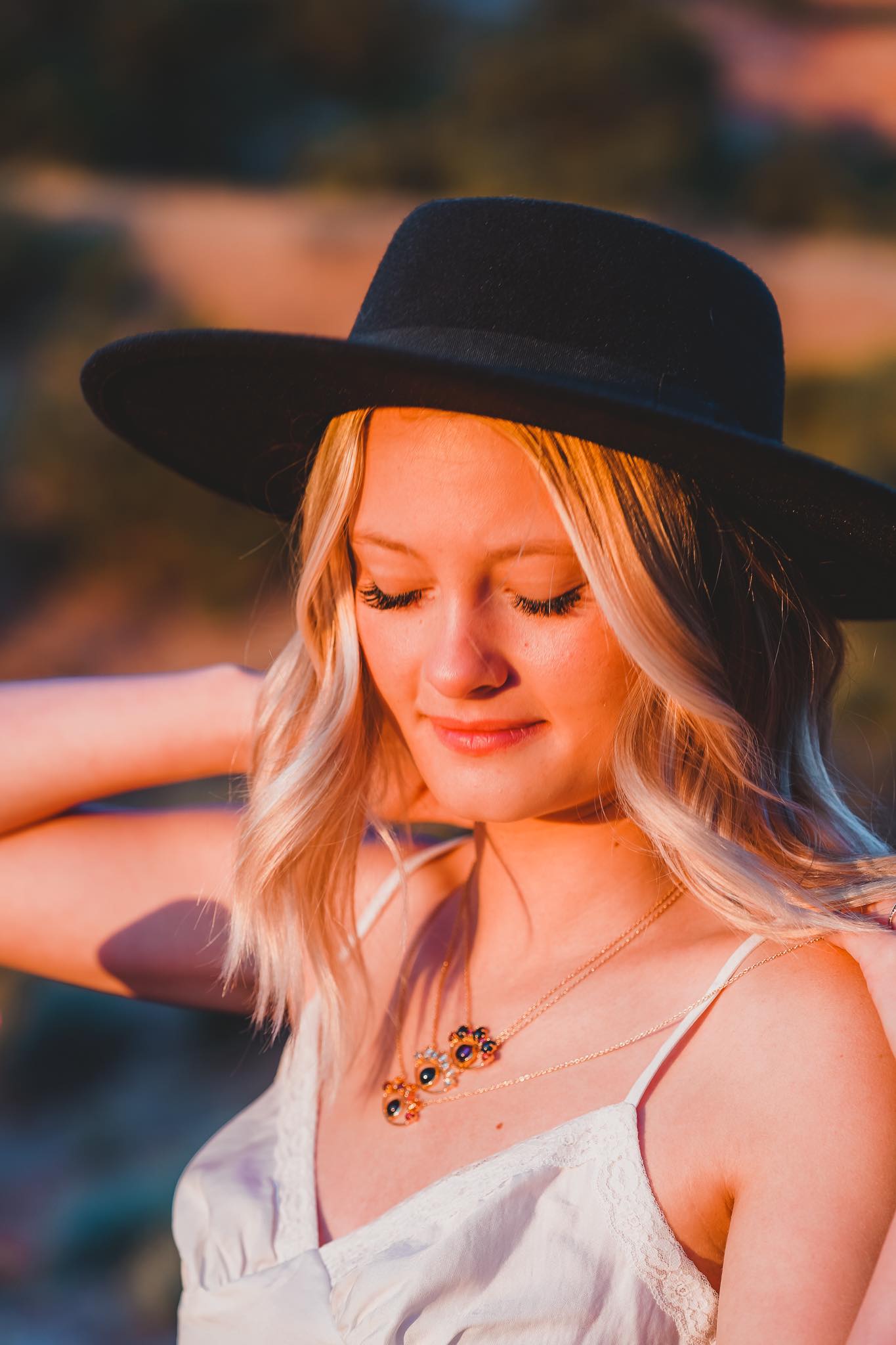 Lifestyle Image of Blonde Girl with Black Hat Wearing Three Evil Eye Necklaces by The Retrograde Shop