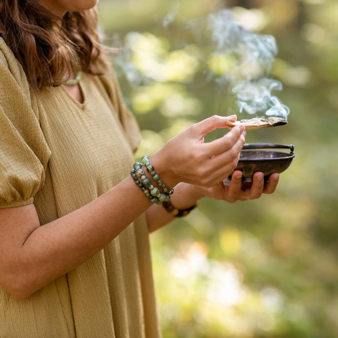 Image of a woman holding a burning palo santo stick in nature